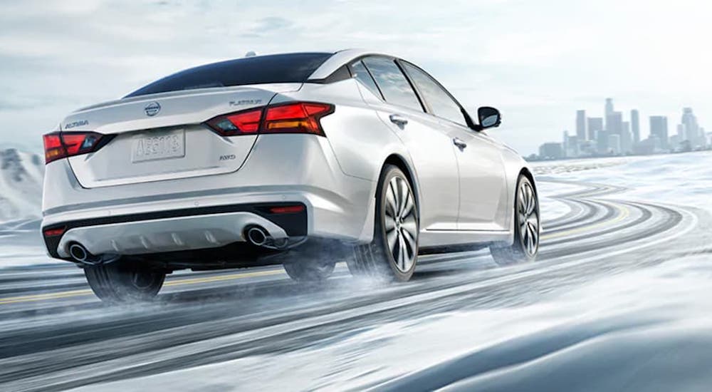 A white 2022 Nissan Altima is shown from the rear while it drives down a snow covered road.