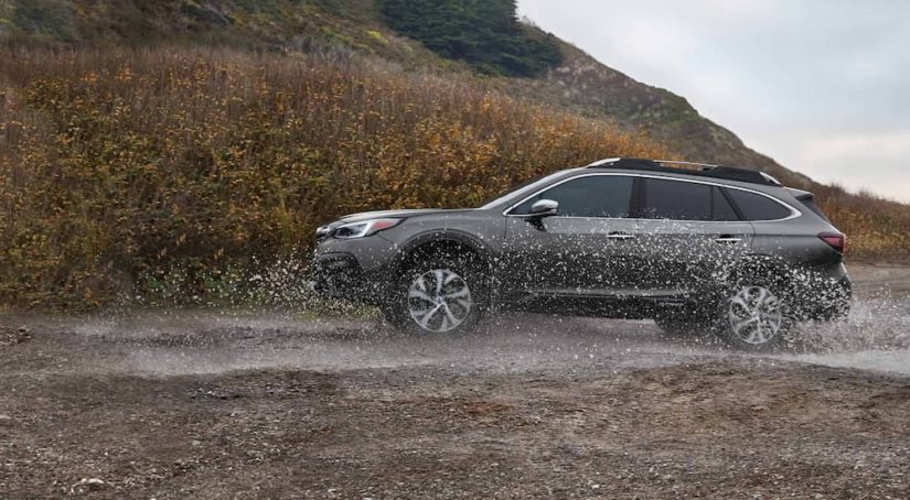 A grey 2021 Subaru Outback is shown from the side while it drives through a puddle after leaving a used Subaru dealer.