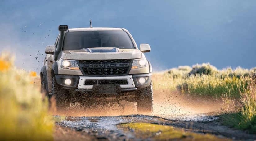 A tan 2022 Chevy Colorado ZR2 Bison is shown driving on a muddy road.