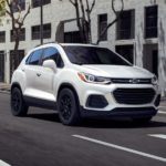 A white 2022 Chevy Trax is shown from the front driving through a city.