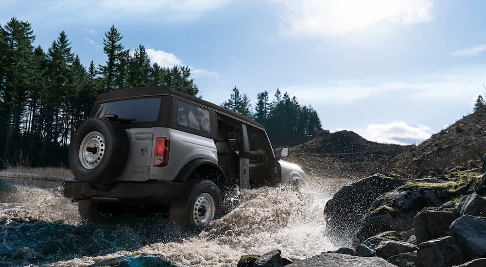 A silver 2022 Ford Bronco Base is shown from a rear angle driving through a river.