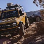 An orange 2022 Ford Bronco is shown off-roading on a rocky trail.