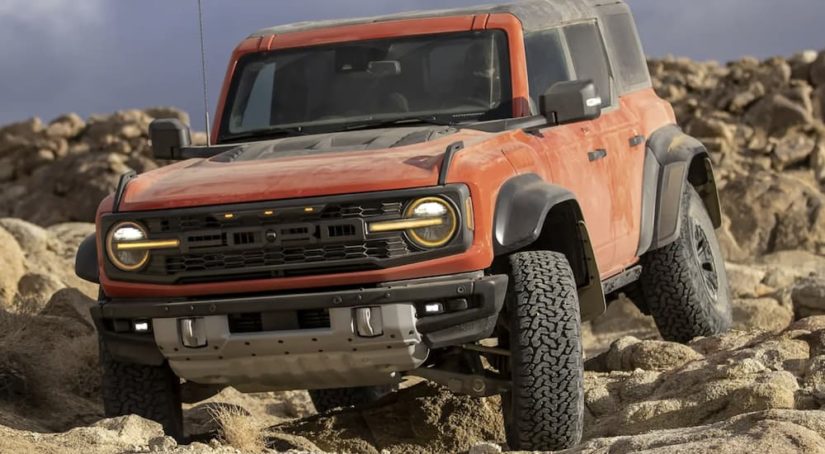An orange 2022 Ford Bronco is shown from the front off-roading on a pile of rocks during a 2022 Ford Bronco vs 2022 Jeep Wrangler comparison.