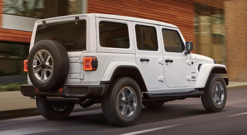 A white 2022 Jeep Wrangler is shown from the rear driving through a city.