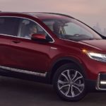 A maroon 2022 Honda CR-V Hybrid Touring is shown from the side parked outside of a city.
