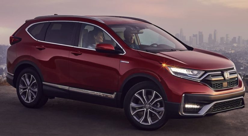 A maroon 2022 Honda CR-V Hybrid Touring is shown from the side parked outside of a city.