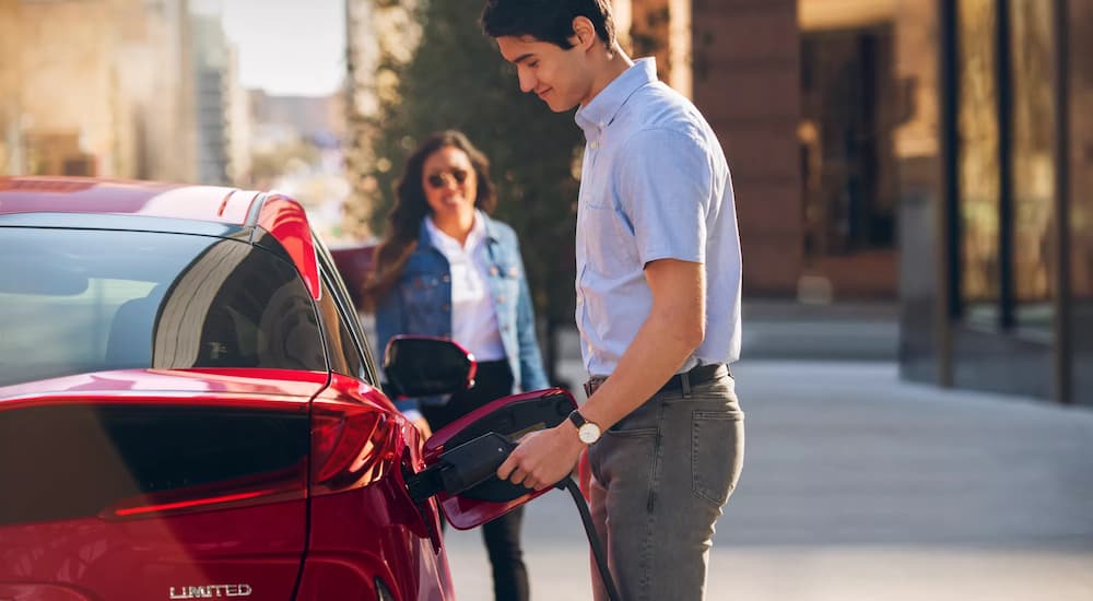 A man is shown plugging a red 2022 Toyota Prius Prime in to a charging station.