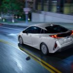 A silver 2022 Toyota Prius Prime is shown from the rear driving on a city street.