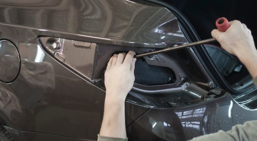 A close up shows a person using a tool on a car for paint dent repair.