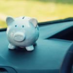 A piggy bank is shown sitting on the dashboard of a vehicle.