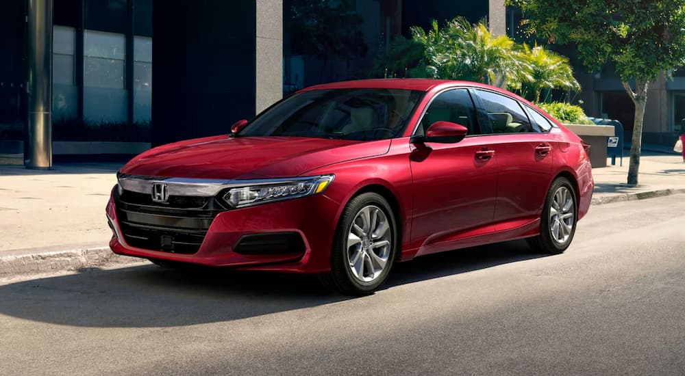 A red 2020 Honda Accord LX is shown parked on the side of a city street near a used Honda dealership.