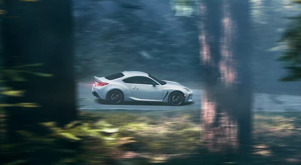 A white 2022 Toyota GR86 is shown from the side as it speeds through the forest during a brand comparison of Toyota and Honda.