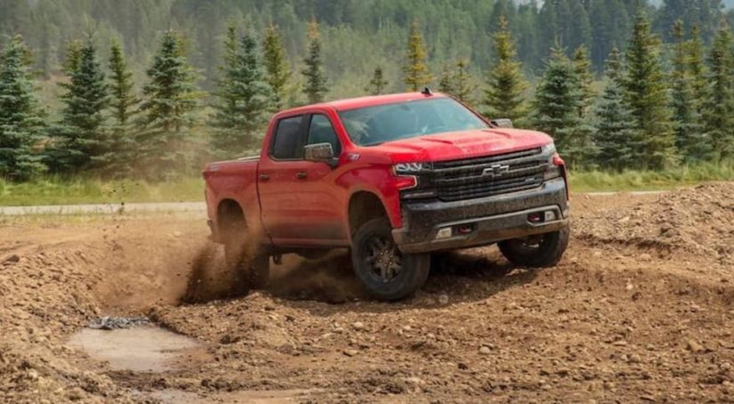 A red 2020 Chevy Silverado 1500 is shown from the front at an angle while it droves through mud after leaving a pre-owned Silverado dealer.