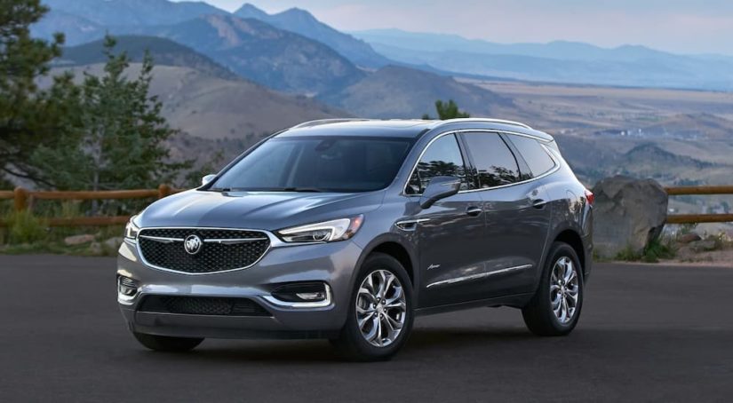 A grey 2021 Buick Enclave Avenir is shown from the front at an angle while parked in a mountainous area.