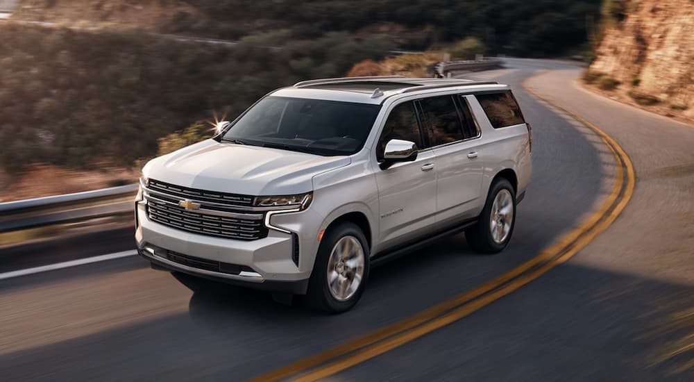 A white 2022 Chevy Suburban is shown from the front at an angle on a canyon road. 