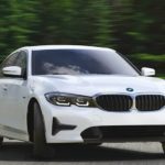 A white 2022 BMW 330e xDrive is shown driving on a forest highway.