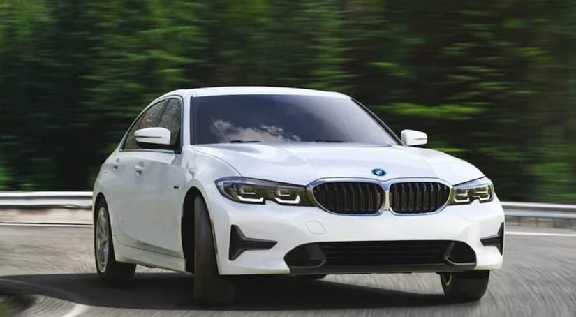 A white 2022 BMW 330e xDrive is shown driving on a forest highway.