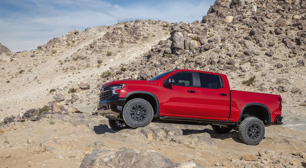 A red 2022 Chevy Silverado ZR2 is shown from the side while it crawls over a rock.