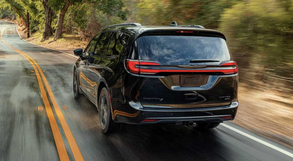 A black 2022 Chrysler Pacifica is shown from the rear driving on an open road.