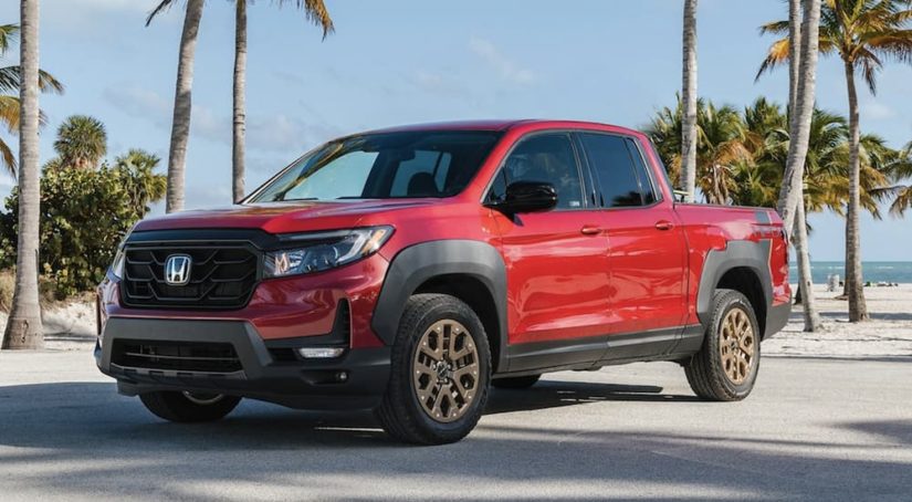 A red 2022 Honda Ridgeline Sport is shown from the side parked around palm trees.
