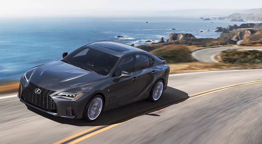 A dark grey 2022 Lexus IS 300 AWD is shown driving on a road near the ocean.