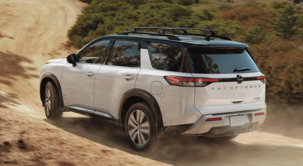 A white 2022 Nissan Pathfinder is shown from the rear driving on a dirt path during a 2022 Nissan Pathfinder vs 2022 Honda Pilot comparison.