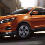 An orange 2022 Nissan Rogue Sport is shown driving on a city street.
