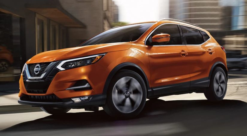 An orange 2022 Nissan Rogue Sport is shown driving on a city street.