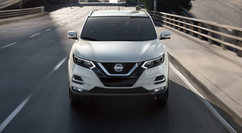 A white 2022 Nissan Rogue Sport is shown from the front driving on an open road.