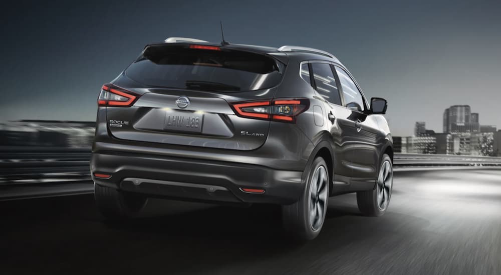 A grey 2022 Nissan Rogue Sport is shown from the rear driving on an open road.