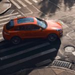 An orange 2022 Porsche Macan S is shown driving on a city street.