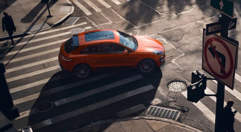 An orange 2022 Porsche Macan S is shown driving on a city street.