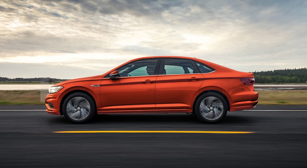 An orange 2022 Volkswagen Jetta is shown from the side driving on an open highway.