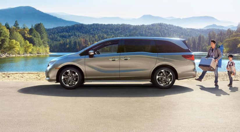 A silver 2023 Honda Odyssey is shown from the side in front of a lake.