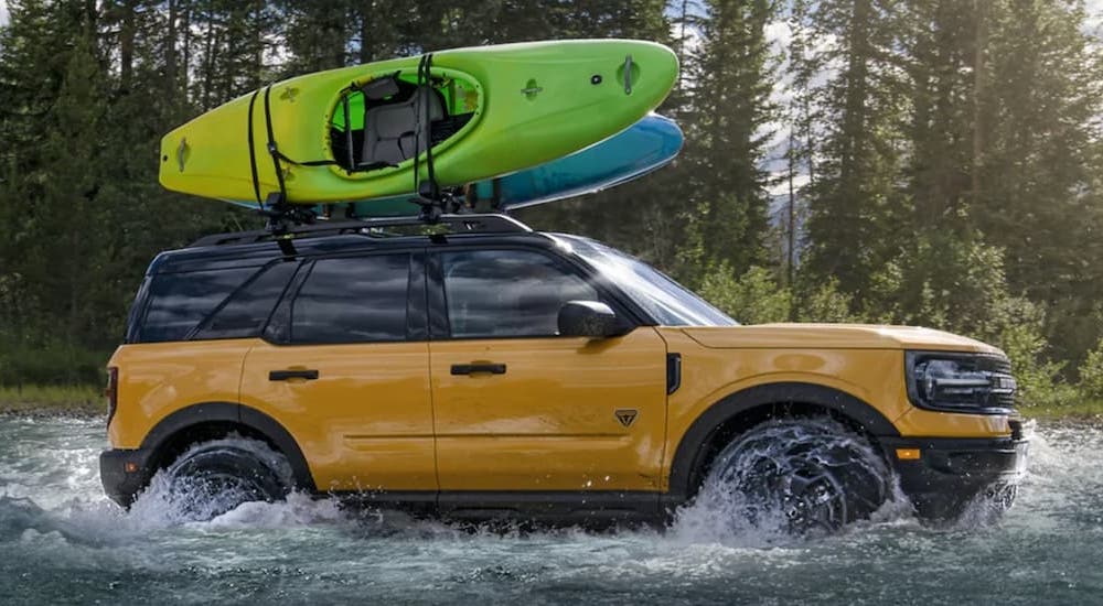 A yellow 2022 Ford Bronco Sport Badlands is shown loaded with kayaks while crossing a river. 