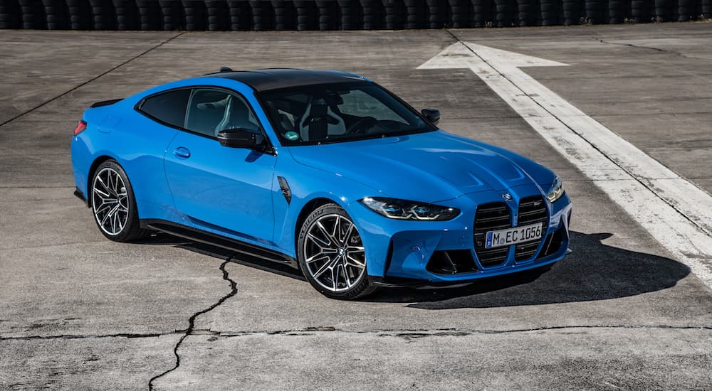 A blue 2022 BMW M4 is shown from the front at an angle while parked on a racetrack.