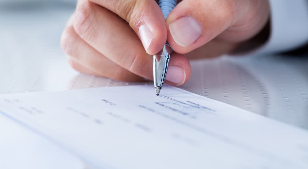 A close up shows a person signing a check.