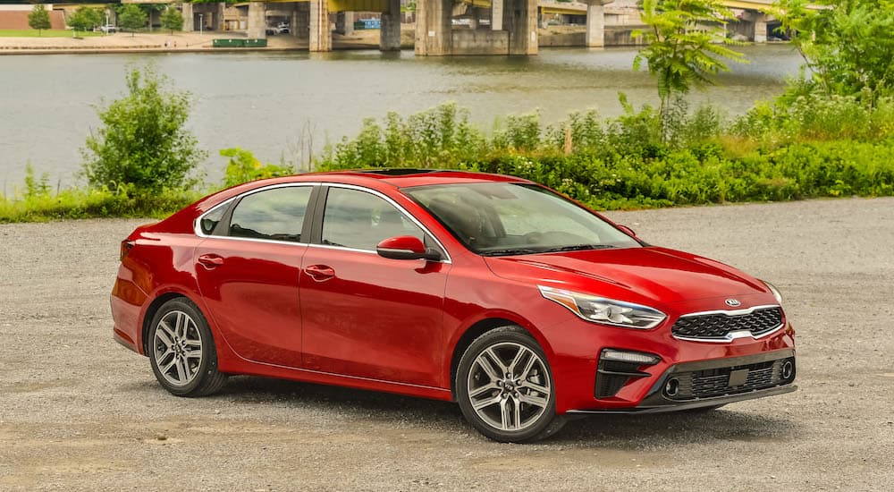 A red 2017 Kia Forte is shown parked by a river and bridge. 