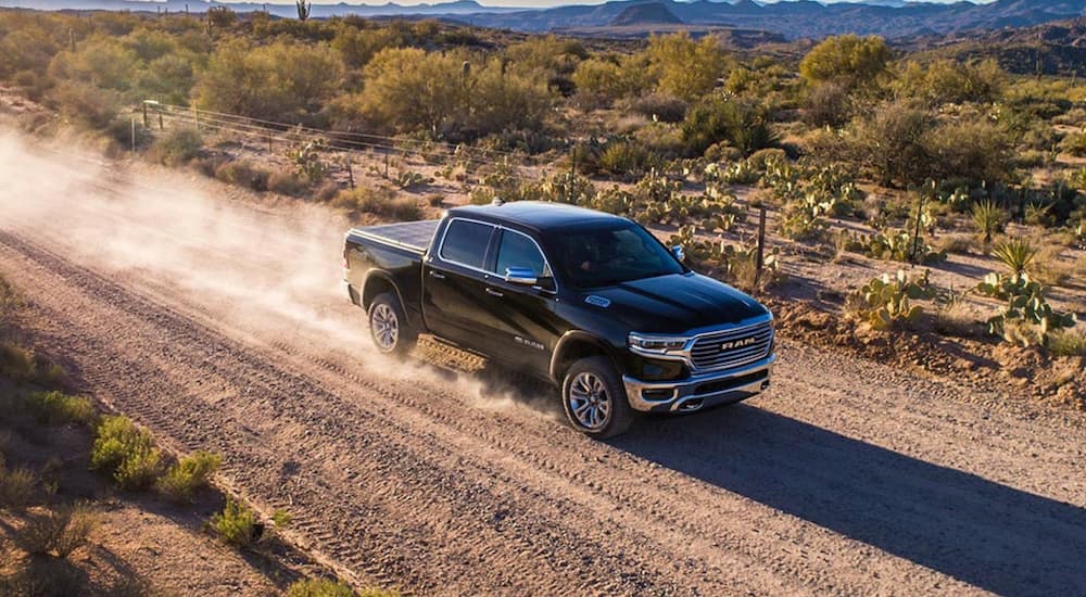 A black 2020 Ram 1500 is shown driving on a dusty dirt road.