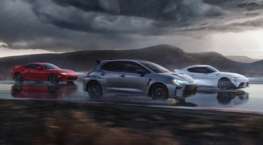 A red 2022 Toyota Gr86, a grey 2023 Toyota GR Corolla, and a white 2022 Toyota GR Supra are shown from the side on a racetrack.