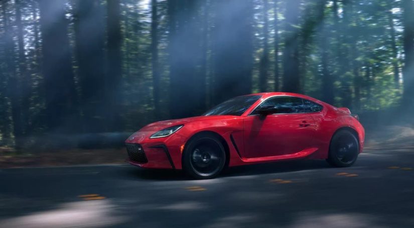 A red 2022 Toyota GR86 is shown from the side while driving through a dark forest.