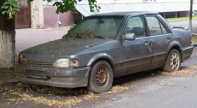 An old grey car is shown parked on a street.