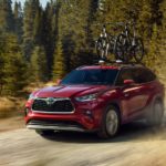 A red 2022 Toyota Highlander Hybrid is shown from the front on a dirt trail while loaded with bikes.