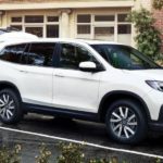 A white 2021 Honda Pilot is shown from the front at an angle in front of a garage during a 2022 Honda Pilot vs 2022 Hyundai Palisade comparison.