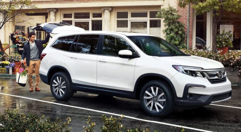 A white 2021 Honda Pilot is shown from the front at an angle in front of a garage during a 2022 Honda Pilot vs 2022 Hyundai Palisade comparison.