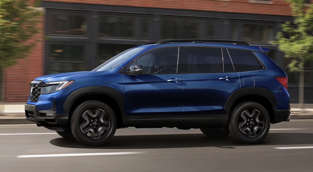 A blue 2022 Honda Passport Elite is shown from the side driving through a city.