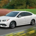 A white 2022 Subaru Legacy Touring XT is shown driving past a field.