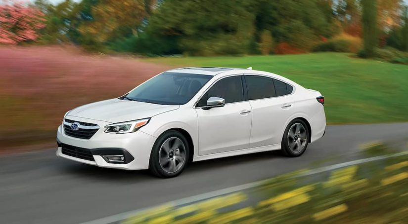 A white 2022 Subaru Legacy Touring XT is shown driving past a field.
