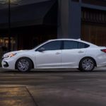 A white 2023 Subaru Legacy is shown from the side driving on a city street.