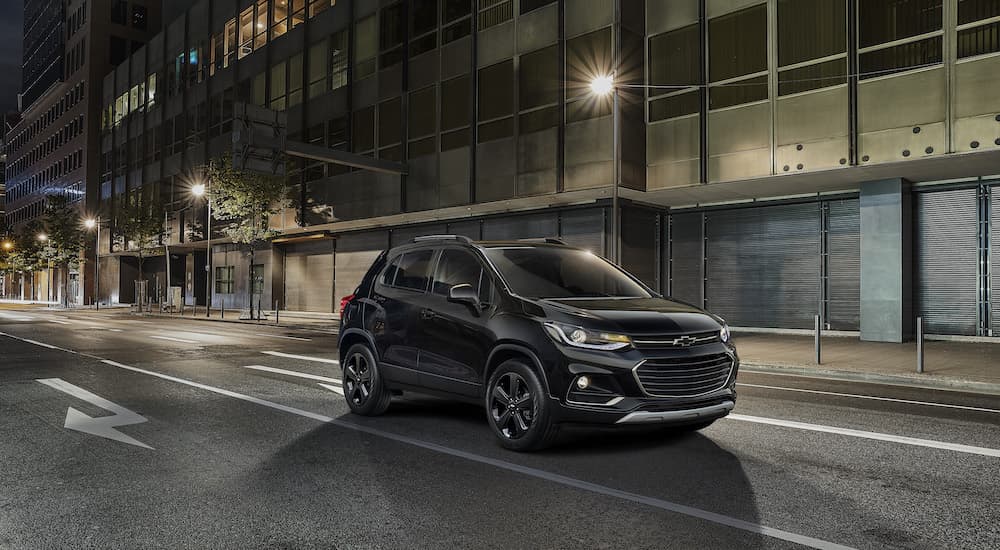 A black 2018 Chevy Trax is shown driving on a city street at night.